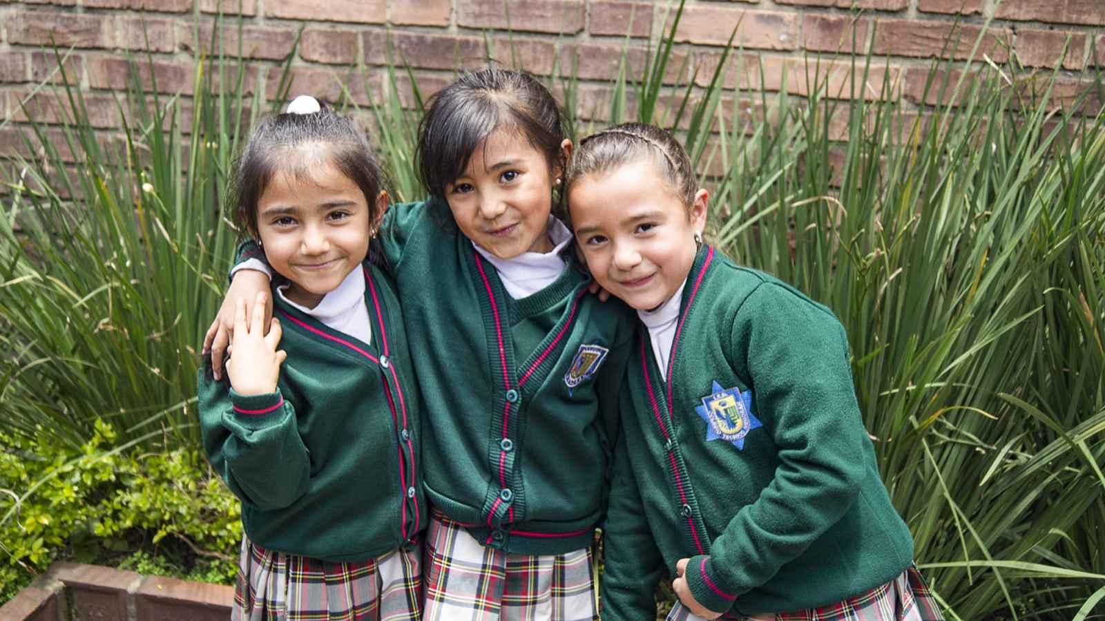 Tres niñas de primaria abrazadas en el jardín del colegio